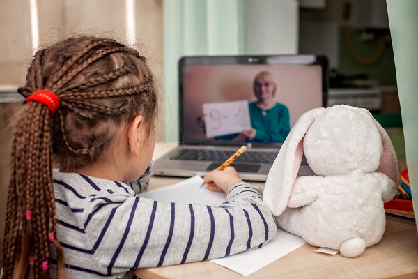 Menina com tranças no cabelo assiste aula pelo computador com seu coelho de pelúcia ao lado